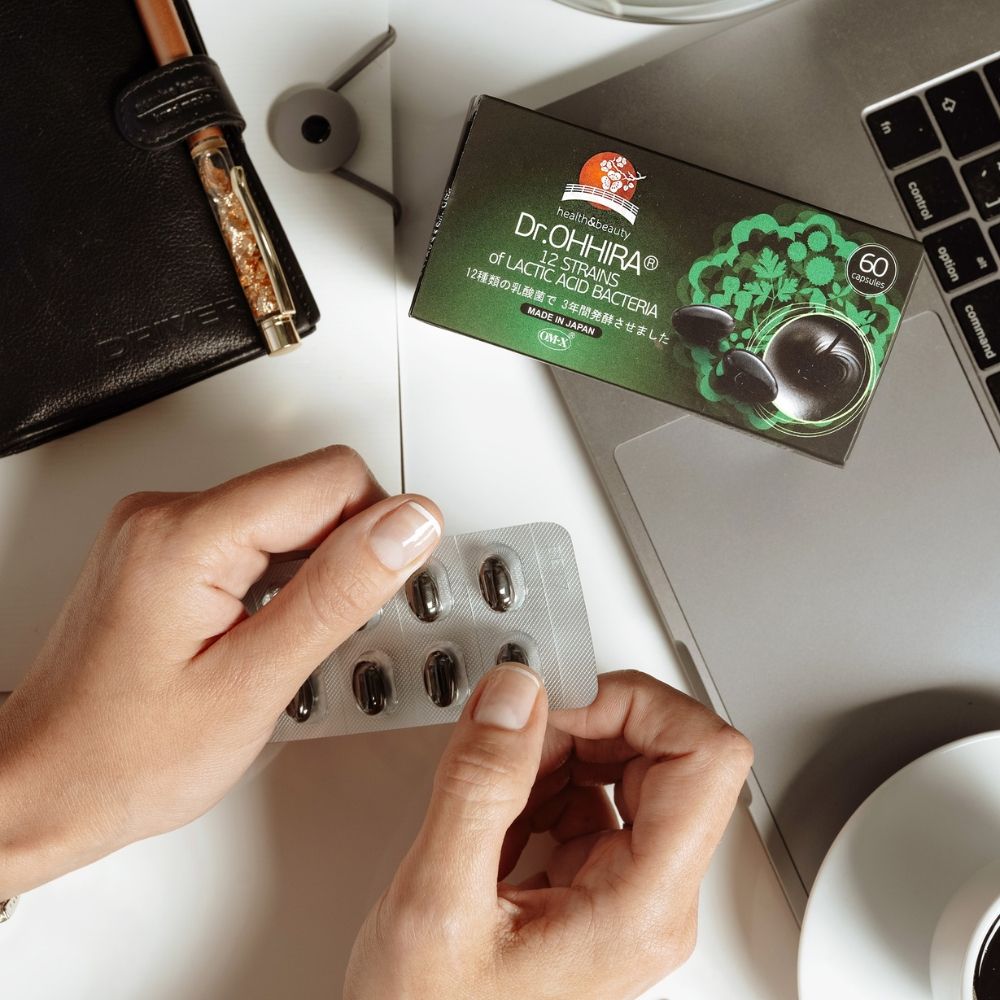 Cutie verde Dr.Ohhira probiotice OM-X® pe birou, lângă laptop, mâini ținând blister capsule.