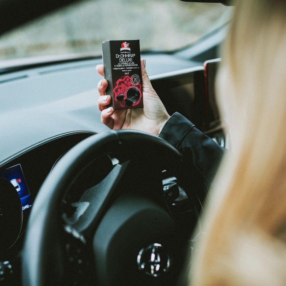 Ambalaj negru Dr.Ohhira® Deluxe probiotice, ținut în mână, interior mașină, detalii capsule negre.