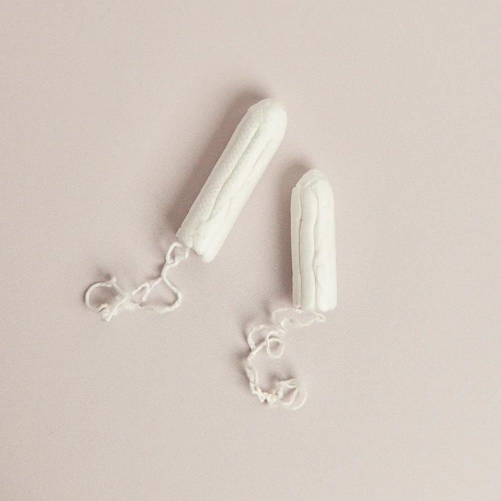 Tampoane bumbac organic alb, textură detaliată, 2 buc. pe fundal roz deschis.