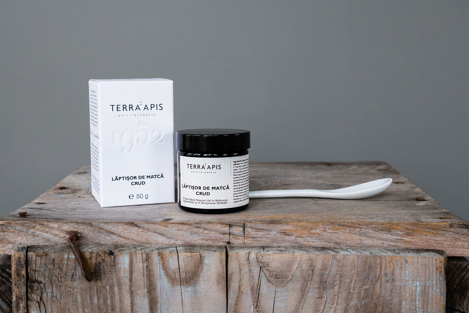 Borcan de sticlă neagră cu lăptișor de matcă crud, 50g, pe un fundal de lemn, alături de cutie albă.