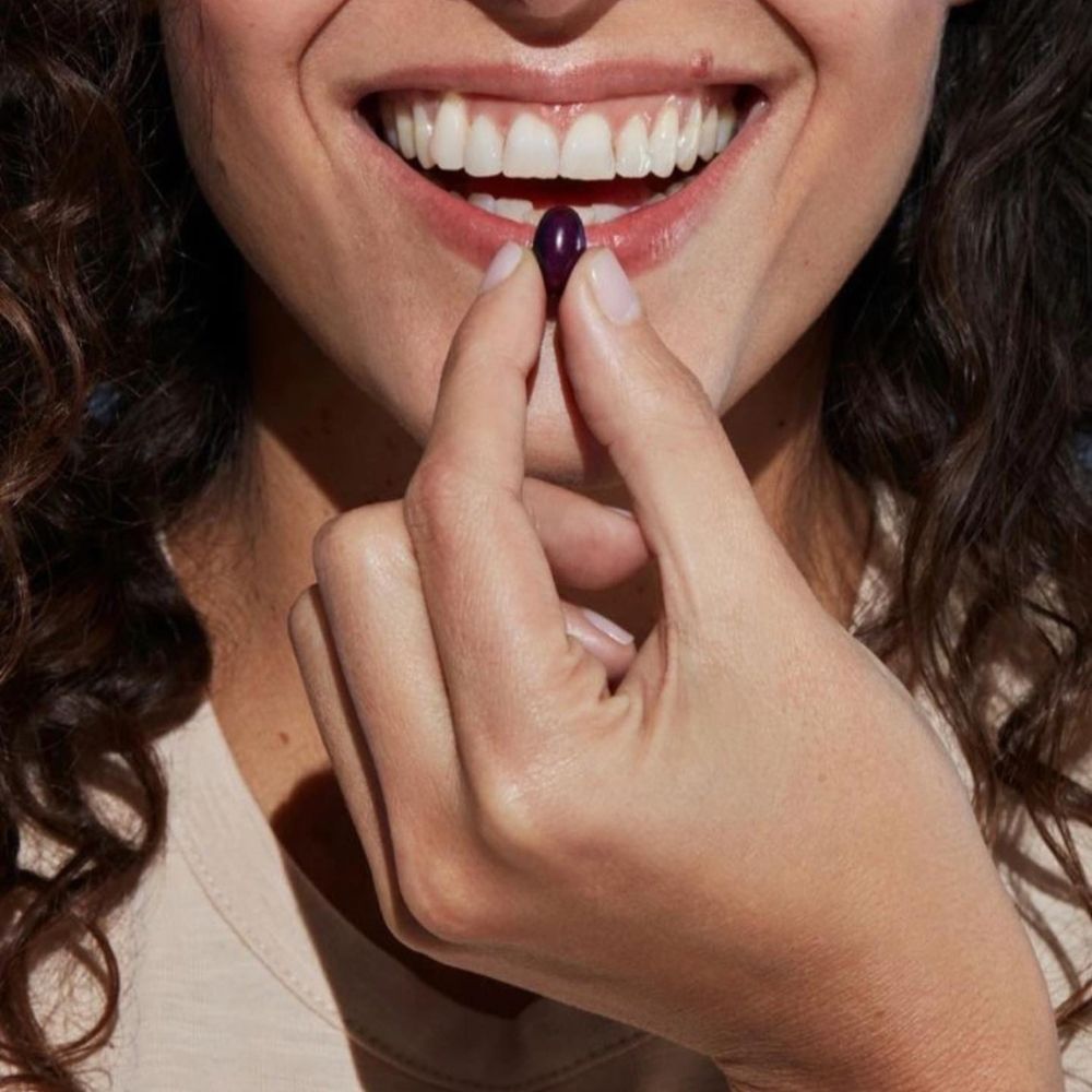 Capsulă Dr.Ohhira® Deluxe probiotic, violet închis, ținută între degete, înainte de consum.