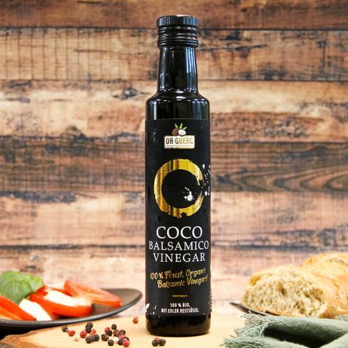 Oțet balsamic de cocos bio 250ml Dr. Goerg, sticlă neagră, etichetă aurie, fundal lemnos.