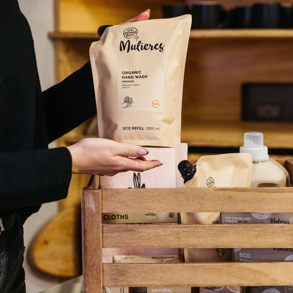 Refill săpun lichid portocaliu Mulieres 1000 ml, ambalaj eco bej în cutie de lemn, mână feminină ținând produsul.